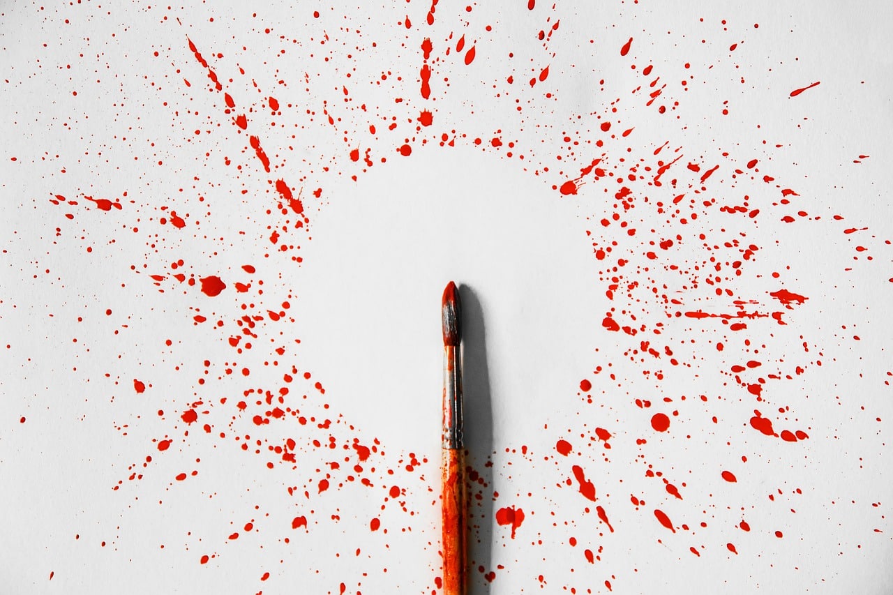 pinceau au milieu d'une feuille avec de la peinture rouge autour